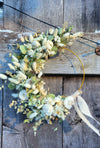 Floral wreath with white flowers and green leaves on a wooden surface