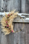 Decorative wreath with dried grasses and flowers on a wooden door with snow.